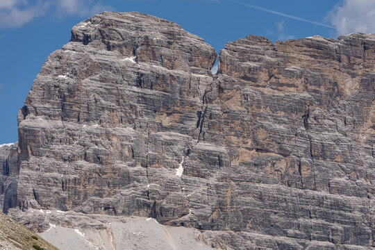 Massive textured dolomites rock wall of a majestic mountain peak under a clear blue sky, wild alpine landscape and extreme climbing destination concept