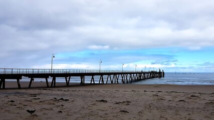Fototapeta premium Adelaide, South Australia - Scenic Wooden Jetty, Calm Ocean, Sandy Shoreline and the Iconic Coastal Atmosphere of South Australia’s Most Popular Beachfront. A panoramic photo of Glenelg Beach.