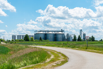 Agricultural grain silos and industrial elevators in a rural landscape. Industrial agriculture: metal grain elevators under a bright summer sky. © ARVD73