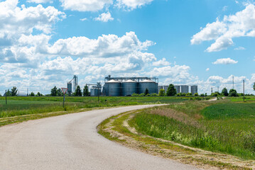 Agricultural grain silos and industrial elevators in a rural landscape. Industrial agriculture: metal grain elevators under a bright summer sky. © ARVD73