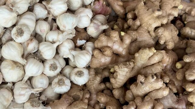 High angle shot of large piles of fresh garlic bulbs and raw ginger roots displayed at a market stall.