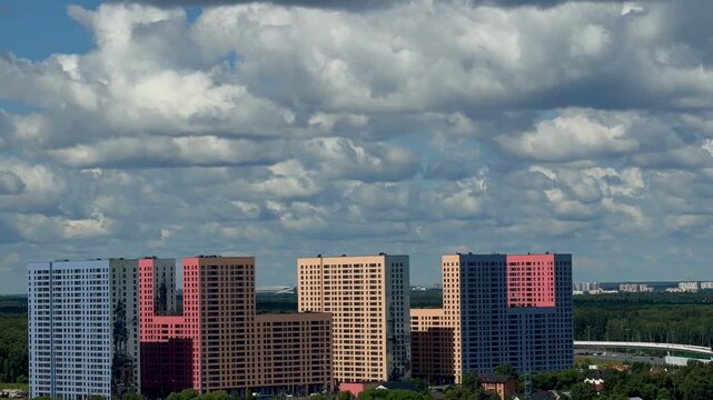 Modern moscow multistory apartment buildings complex cloudscape. Voluminous fluffy clouds flying fast over bright residential block panels, city road traffic flows and suburban highway lines.