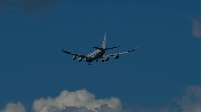 Close up of passenger airplane flying in blue sky. Commercial four-engine airliner with landing gear down descending for arrival above fluffy white cumulus cloudscape in steady real time video.