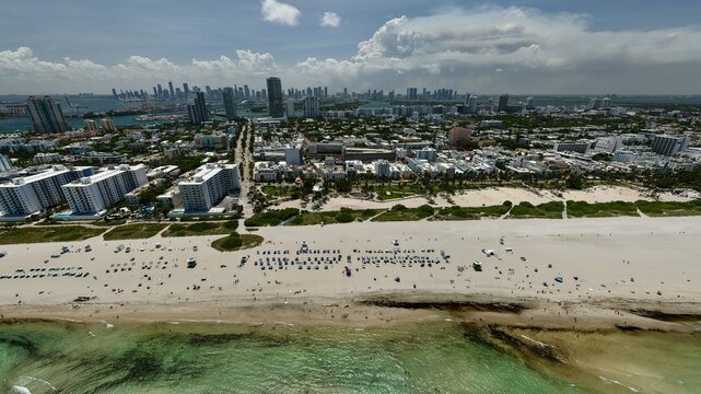 Aerial view of South Beach featuring white sand, turquoise ocean waters, rows of beach umbrellas, and the city skyline in the background, Miami Beach, Florida, United States.