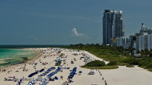 Aerial view of South Beach with white sand, blue ocean water, rows of blue umbrellas, and high-rise buildings along the coastline in Miami Beach, Florida, United States.