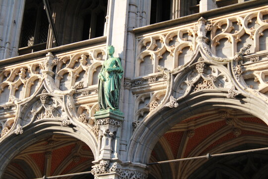 Detail of ornate Brabantine Gothic stone tracery and a green patinated bronze statue on a historic facade at the Grand Place in Brussels, Belgium, in warm sunlight
