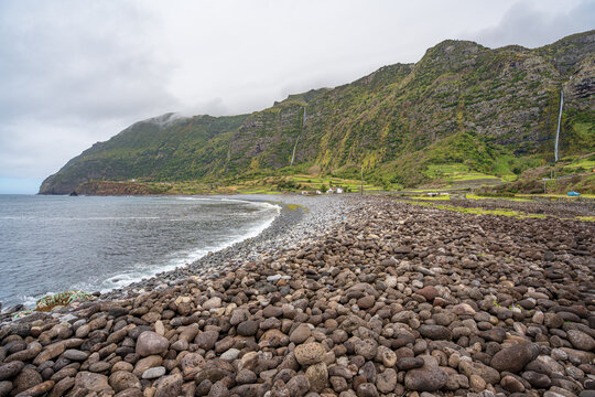 Beach with round stones, framed by waterfalls in Faj&atilde; Grande. Flores Island, Azores, Portugal.