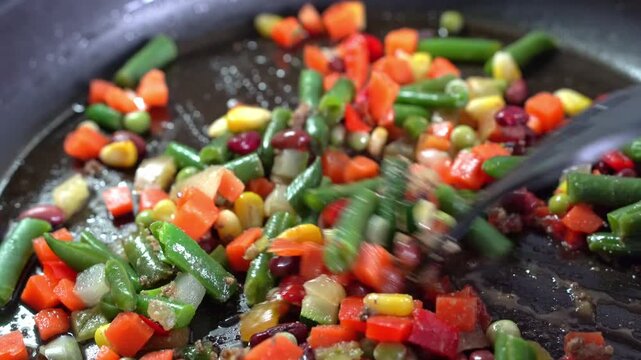 A close-up of vegetables being cooked in a frying pan. Healthy eating. A person stirs the mixture with a spatula.