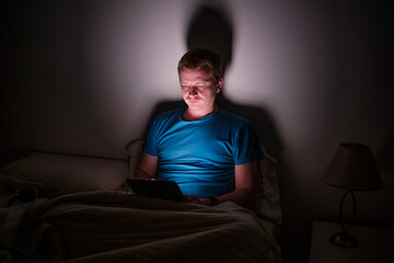 Fototapeta premium Man using tablet in bed suffering insomnia blue light