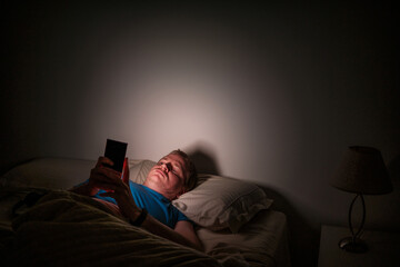 Fototapeta premium Man experiencing insomnia using smartphone in dark bed
