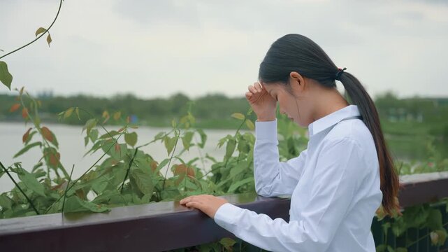 Confused young businesswoman deep in thought while leaning against a wooden railing, suffering from anxiety and headache due to overwork, multitasking, and difficult deadlines