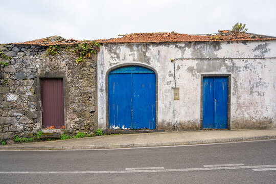 Rustic whitewashed house with blue doors and windows, attached to a rustic stone house.
