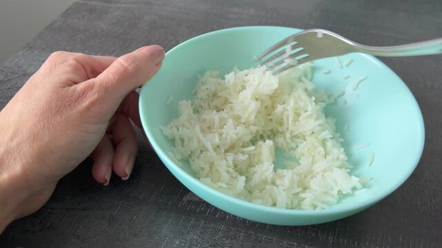 A woman&rsquo;s hand is stirring the rice in a plate with a fork. The idea is that the ration is meagre.