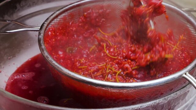 Cooking redcurrant jam process of mashing berries through a metal sieve. A chef uses a spatula to extract pure juice. Fresh preparation in a glass bowl. Close up view of making confiture.