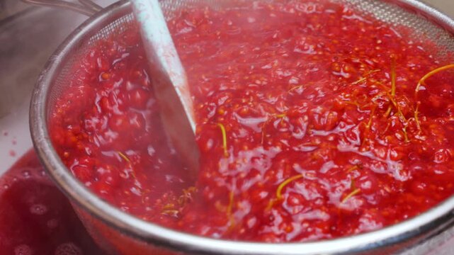 Cooking redcurrant jam process of mashing berries through a metal sieve. A chef uses a spatula to extract pure juice. Fresh preparation in a glass bowl. Close up view of making confiture.