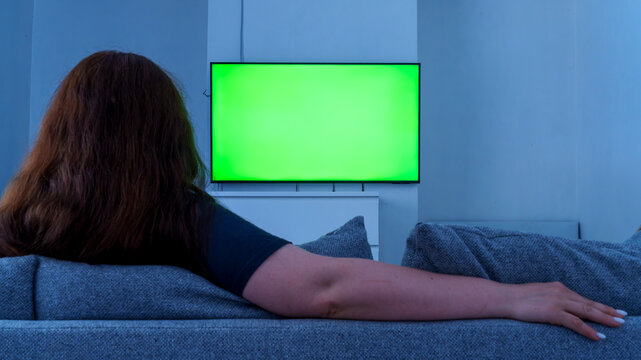 Woman watching tv with green screen at home