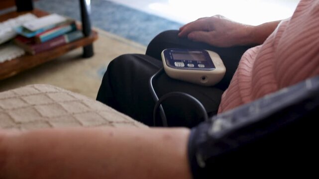 Elderly woman at home checking her blood pressure with a monitor. Ideal for health, medical care, and home assistance concepts