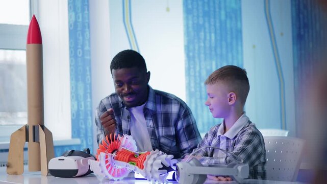African American mentor and child assembling colorful 3d printed turbine engine and rocket model on table in stem classroom.