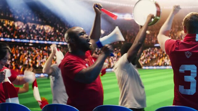 Excited football supporter beats drum among fans walking in packed stadium during match day, showing fan leader creates rhythm for loud crowd to chant with vuvuzelas and megaphone.