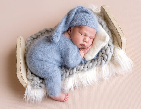 Newborn baby sleeps peacefully in tiny bed during a studio session. Professional newborn photoshoot.