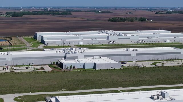 Backward drone shot revealing a hyperscale data center campus surrounded by agricultural land on a clear day.