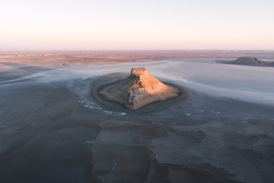 Aerial view of the Karynzharyk mesa rising from the vast salt flats of the desert landscape under soft morning light in Karakiya District, Mangystau Region, Kazakhstan.
