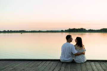 Fototapeta premium Couple enjoys a serene sunset by the lake, sitting on a wooden pier