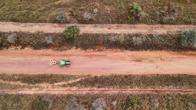 Tractor pulls tyres over dirt sand road to scrape and level it. Overhead drone