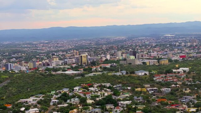 Aerial view across the central business district of Windhoek with modern high-rise buildings among green hills. A sprawling capital ringed by highland mountains.