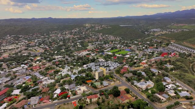 Wide drone cityscape of Windhoek with residential neighbourhoods and roads reaching the mountain horizon. A sprawling capital ringed by highland mountains.