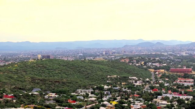 Drone panorama of Windhoek capital city with the central skyline and forested hills in the foreground. A sprawling capital ringed by highland mountains.