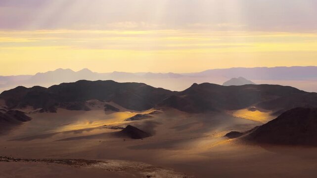 Aerial over the Namib desert at sunrise with golden light raking across dunes and layered mountains. Soft light and drifting mist wrap the ancient dunes and mountains in a calm cinematic atmosphere.