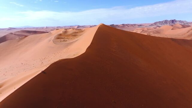 Drone view of a massive star-shaped red dune in the Sossusvlei dune sea of the Namib desert. The towering red dunes glow against the pale cracked clay pans of this ancient desert wilderness.