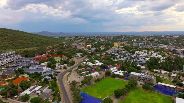Drone view over Windhoek showing residential streets, a green sports field and the surrounding hills. A sprawling capital ringed by highland mountains.