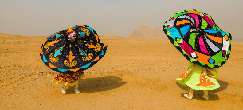 Two joyful Egyptian tanoura folk dancers spinning vibrant colorful skirts in the Giza desert before the ancient pyramids ideal for Egypt tourism and
