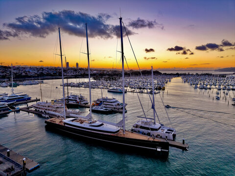 Aerial view of the Wynyard Quarter marina featuring a large luxury sailing yacht moored at the pier during a vibrant sunset with boats in the background in Auckland, Auckland, New Zealand.