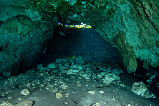 Cenote cave tunnel leading toward a bright opening with sunlight entering underwater