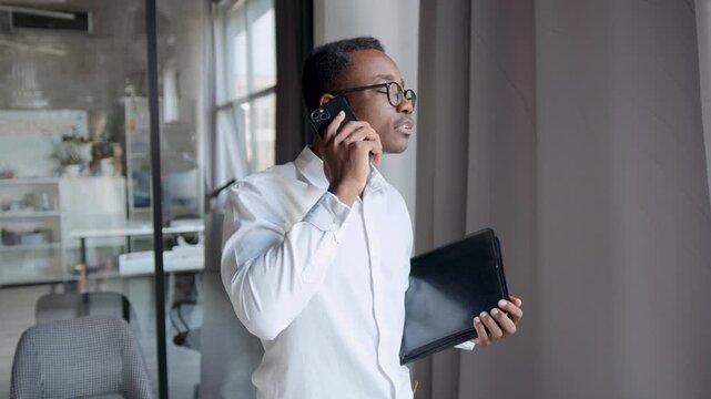 Man in office has intense conversation on smartphone while holding a laptop, trying to express his point in an argument during a busy workday