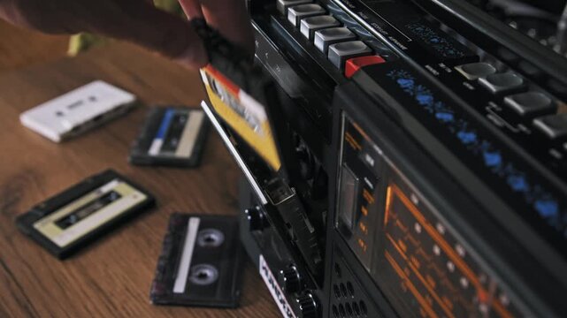 A hand presses the eject button on a vintage black boombox and removes a cassette tape. Several tapes lie on the wooden table. This concept highlights nostalgia for retro audio technology.