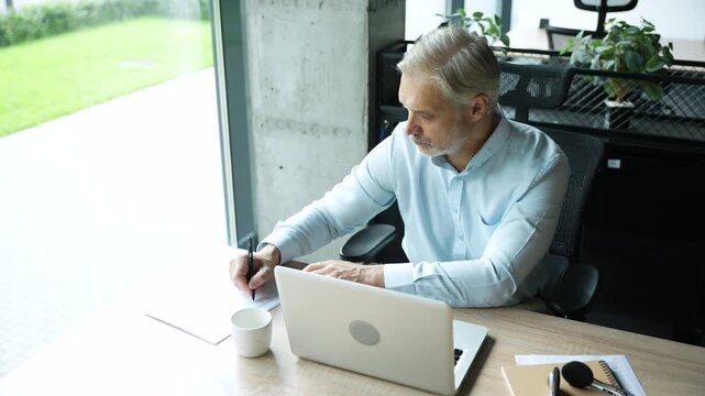 Mature 40s focused businessman, executive director working using laptop, doing data base online research sitting at office. Successful business man, leader, ceo manager, trader trading crypto currency