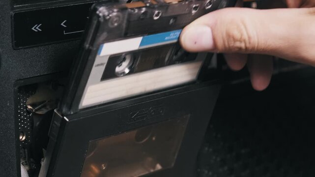 Close-up of a hand operating a vintage boombox by ejecting and re-inserting a cassette with a blue label. The closing deck and pressing of the play button demonstrate the use of 80s audio equipment.