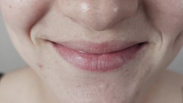 A young woman's mouth curves into a gentle smile in extreme close-up, revealing natural skin texture and distinct pores. Concept of authentic beauty and positive human emotions.