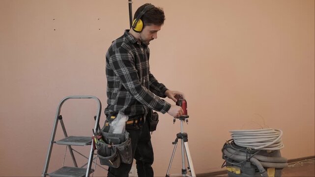 Worker uses self leveling laser level to mark walls before chasing for new electrical wiring installation in room