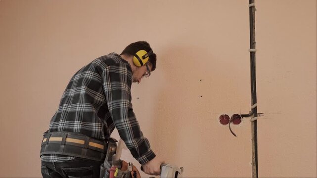 Electrician descending ladder after wall chasing with a wall chaser tool completing wall preparation for electrical wiring installation in apartment renovation