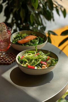 Healthy green salad with shrimp strawberry and avocado served in a bowl on a cafe table with a dragon fruit cocktail