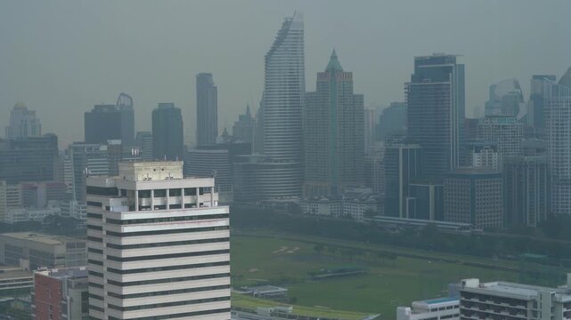 Tilt down aerial view of a modern city skyline with dense skyscrapers covered in heavy smog and toxic air pollution revealing a sports club