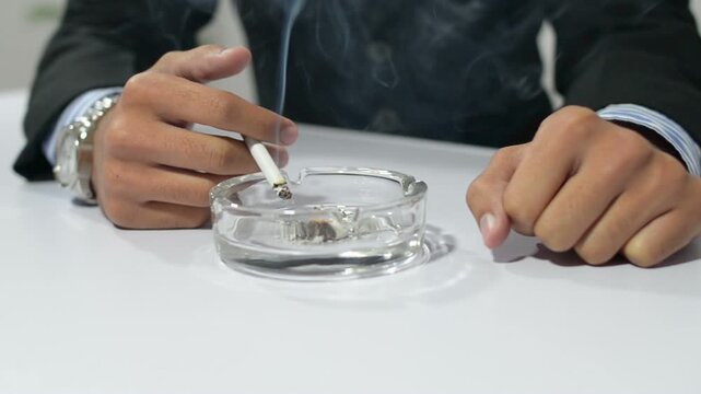Person holding a lit cigarette over an ashtray with visible smoke. Concept of tobacco addiction, nicotine dependence, smoking habit, health risks, lung disease prevention, and unhealthy lifestyle.