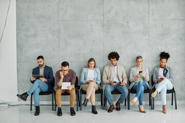 Fototapeta premium Portarit of a group of young business people using mobile phones waiting to apply for a job in the office