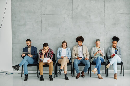 Portarit of a group of young business people using mobile phones waiting to apply for a job in the office