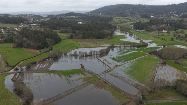 Aerial view of river flooding covering green fields and an eco trail in Portugal.